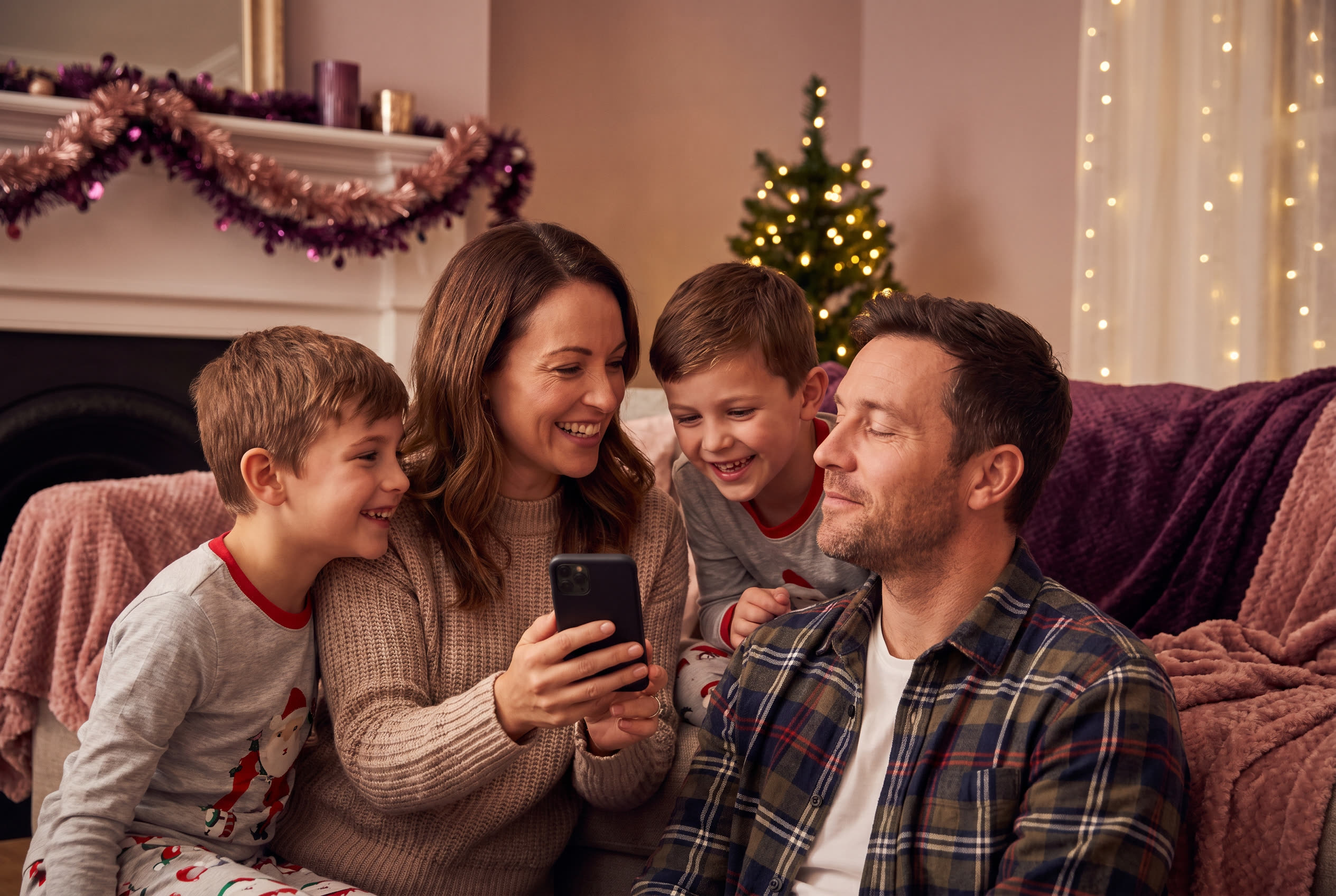 A family playing a song from a smartphone for their husband during a christmas celebration, everyone listening with delighted smiles