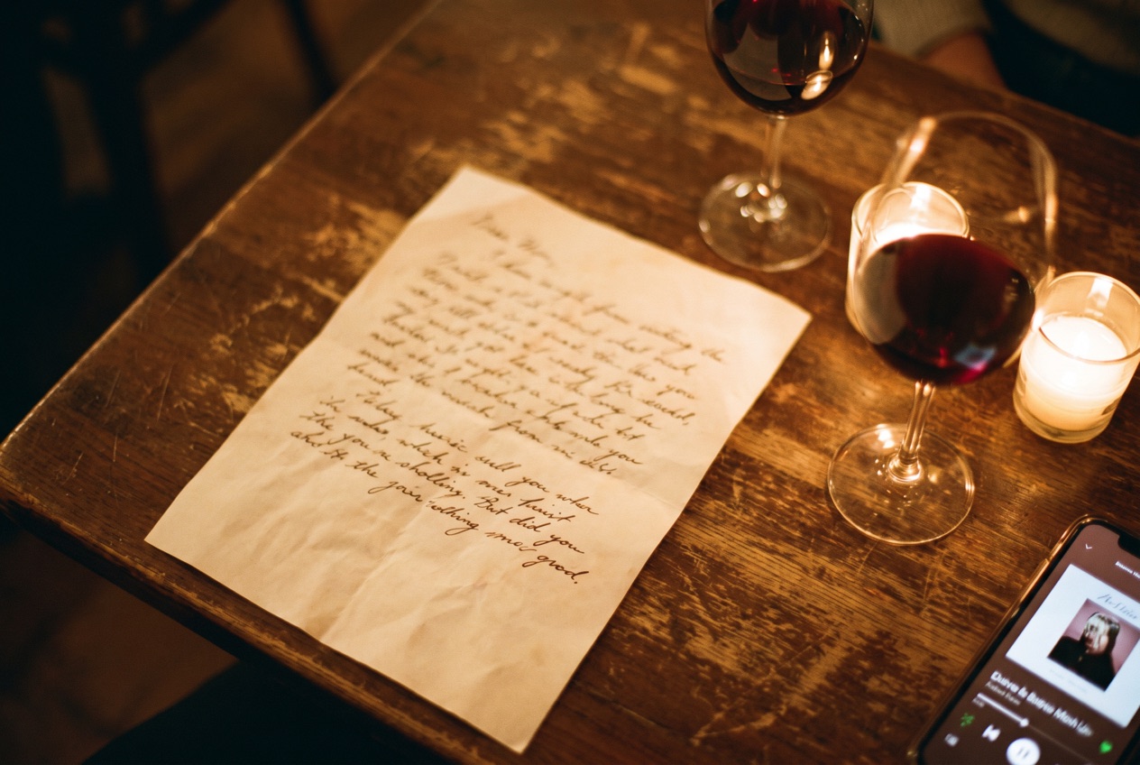 Handwritten anniversary song lyrics beside two glasses of wine and a lit candle